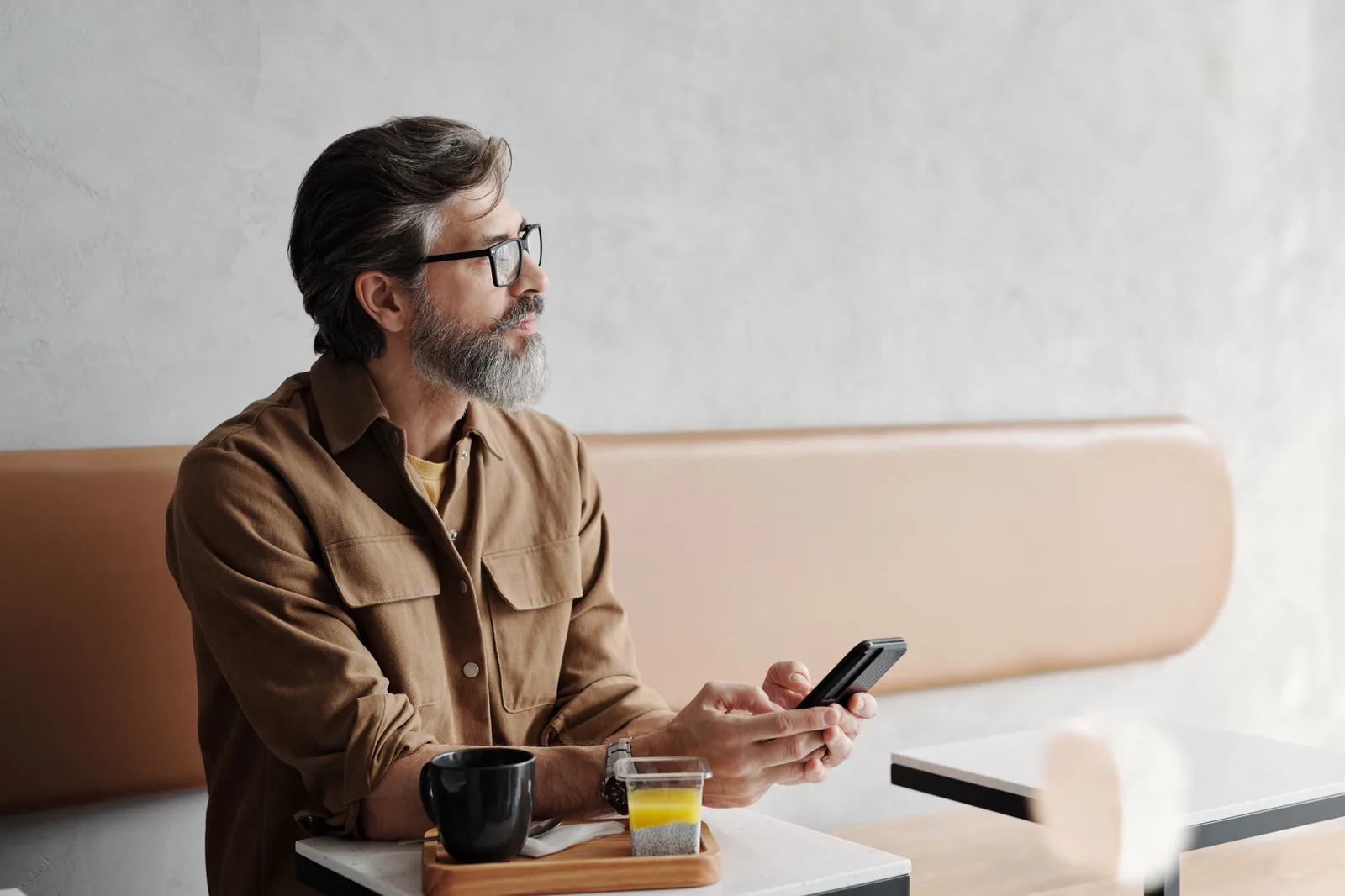 Ein Mann mit Bart sitzt in einem Café, hält sein Smartphone in der Hand und wartet, bis die Seite geladen ist.